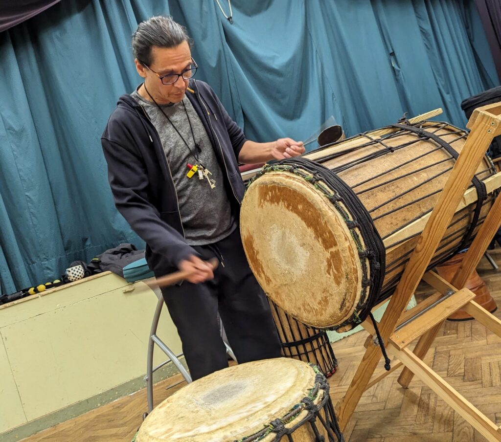 A man hitting a large African bass drum with a stick