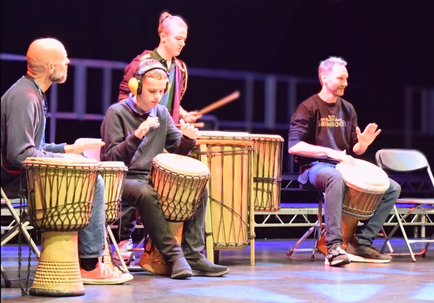 two adults and two children performing African drums on stage